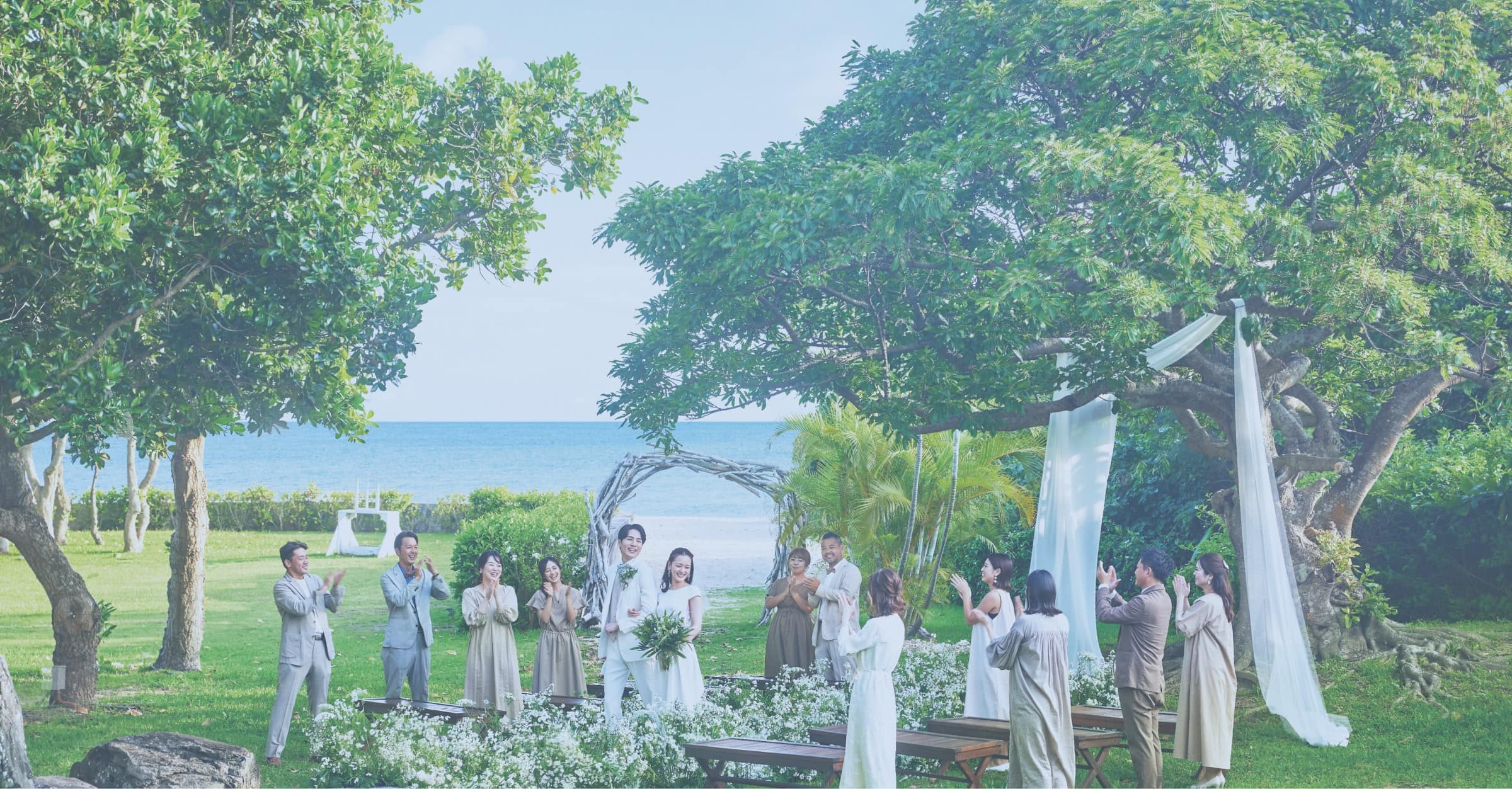 ガーデンウエディングの会場で、両サイドの参列者に祝福されながらバージンロードを歩く新郎新婦