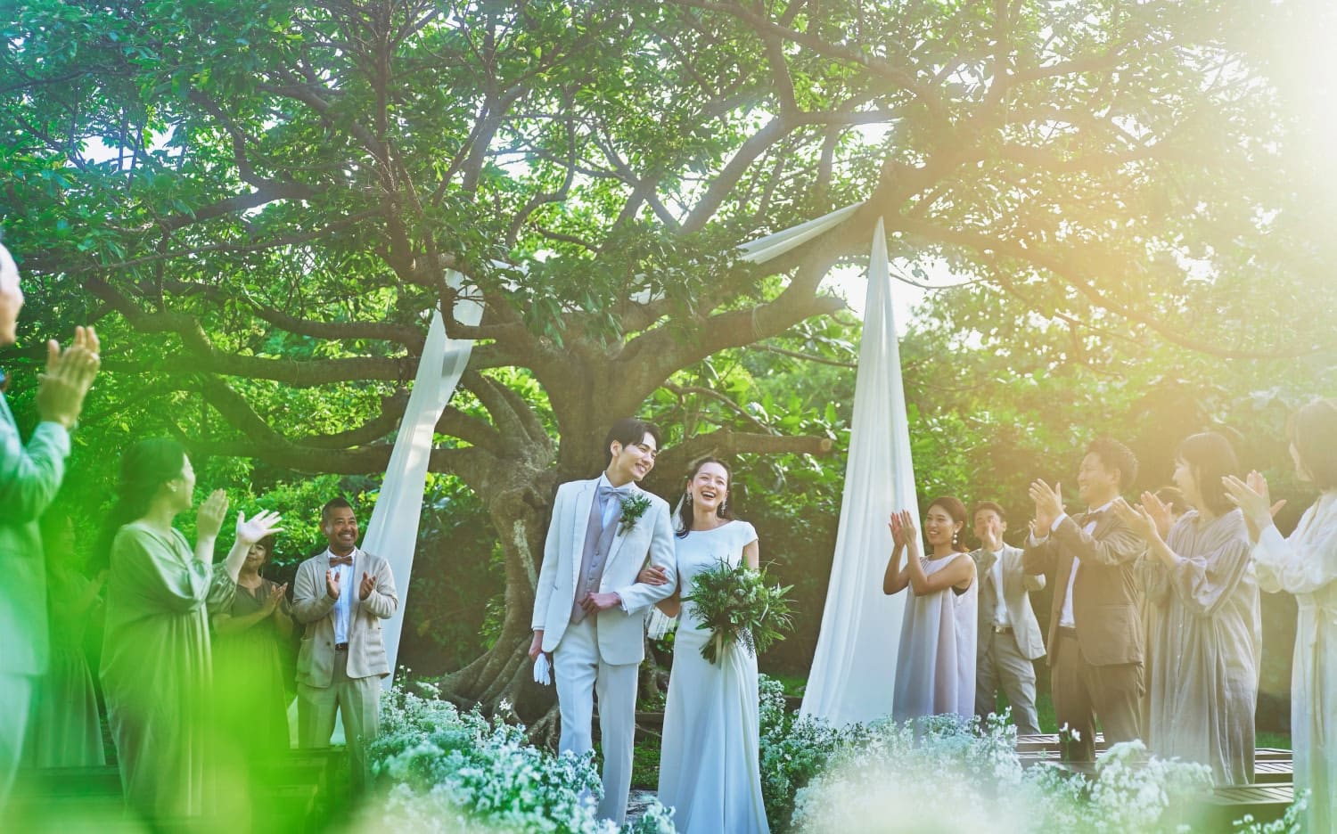 沖縄の緑豊かな自然に囲まれたガーデンウエディングで、幸せそうに微笑む新郎新婦と参列者たち