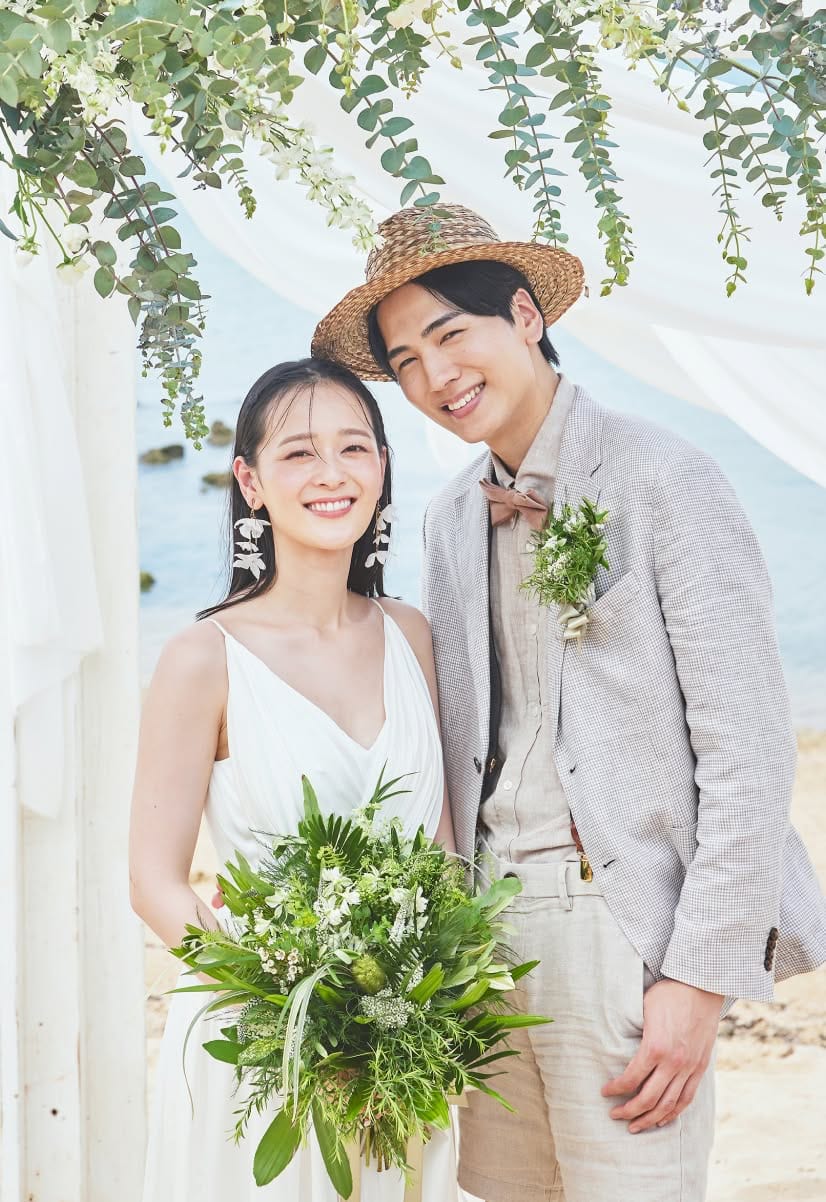 美しいビーチを背景に、ウエディングフォトの撮影でカメラに向かって微笑む新郎新