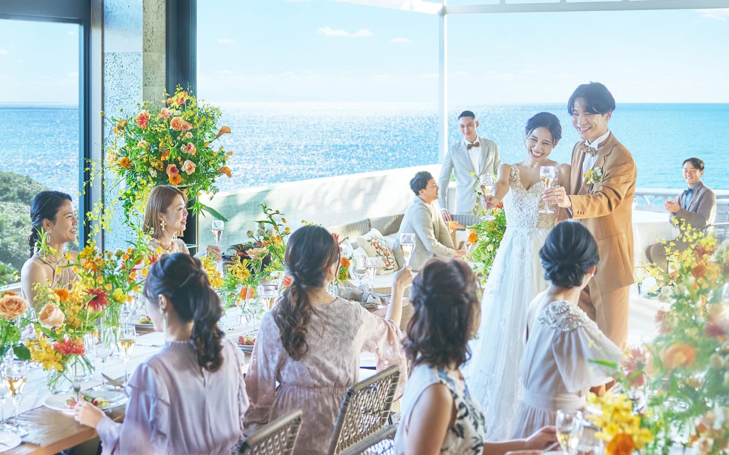 沖縄の海を背景にテラスで披露宴を行う新郎新婦とゲストの皆様
