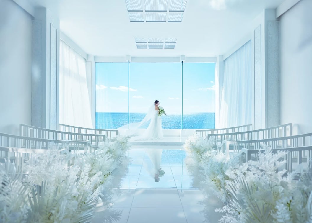 白を基調とした挙式会場で、風にベールやドレスをなびかせながら、ブーケを持って静かに佇む花嫁
