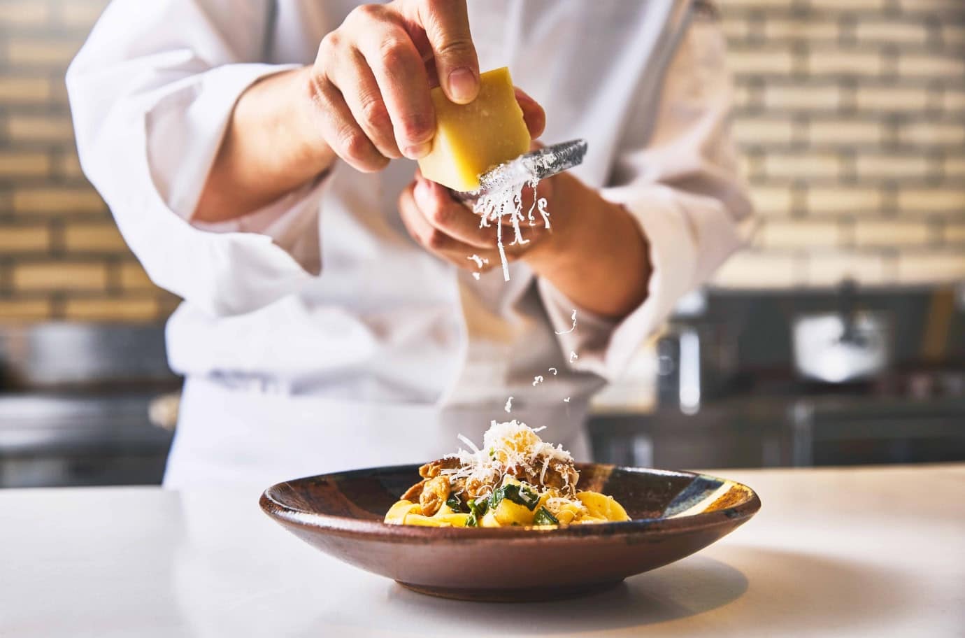 シェフがゲストの目の前で、湯気が立つ熱々のパスタにチーズを削りかけて仕上げている、ライブ感あふれる演出の様子