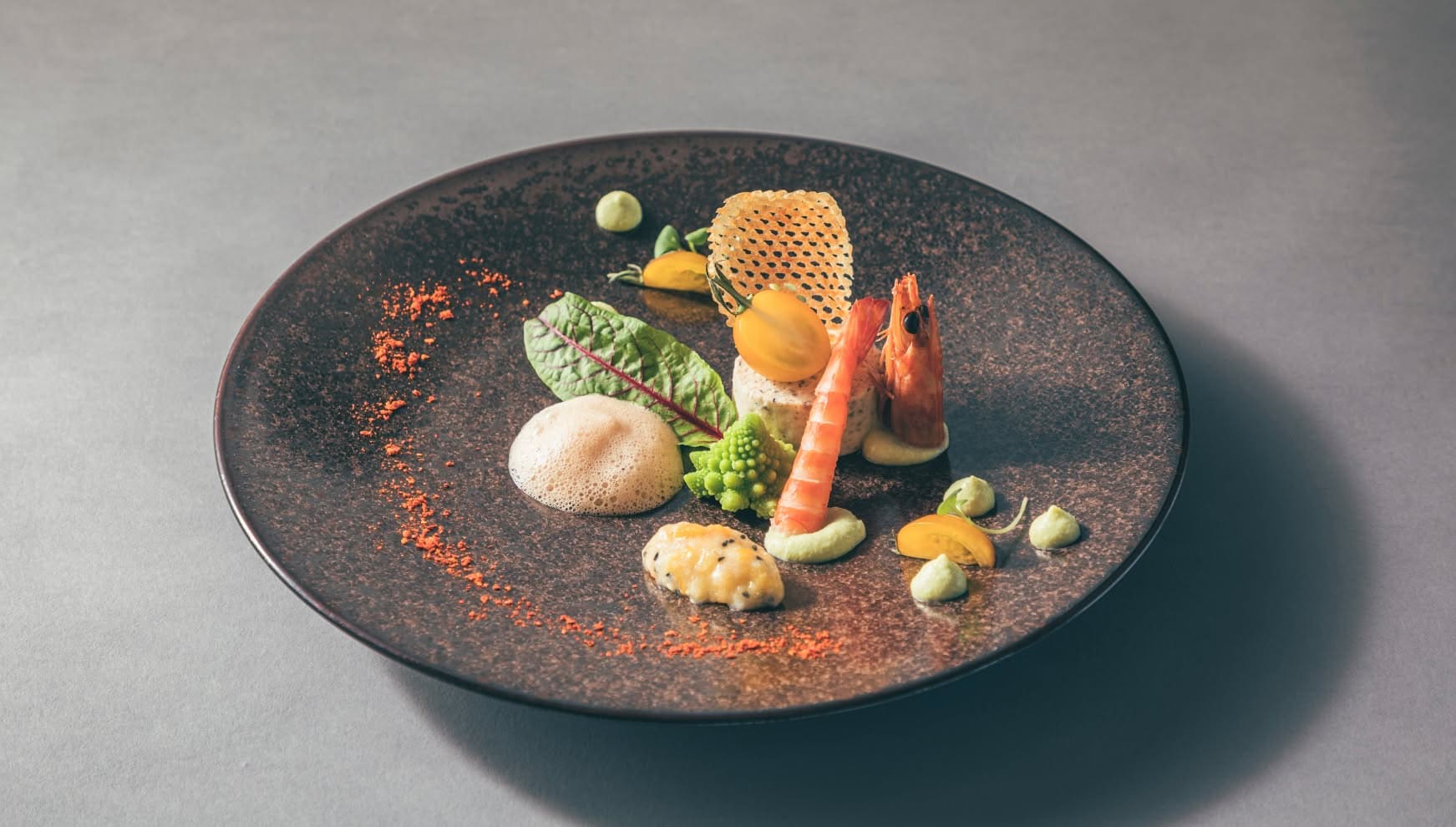 シックな黒いプレートに盛り付けられた、海老のポワレとロマネスコのウエディングメニュー。クリーミーな泡のソースや鮮やかな野菜、香ばしく焼かれたチュイールが添えられた、沖縄の披露宴を彩る洗練されたフレンチの一皿。