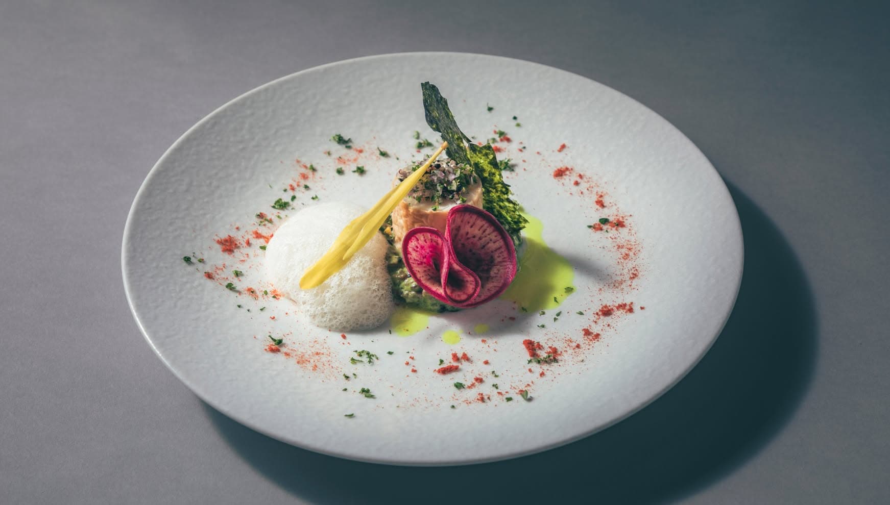 白い円形プレートに美しく盛り付けられた、アイネス ヴィラノッツェ 沖縄のウエディングメニュー。ふんわりとした白い泡のソース、鮮やかな赤紫の紅芯大根、エディブルフラワーが添えられ、周囲に散らされたスパイスが華やかさを演出する繊細な一皿。