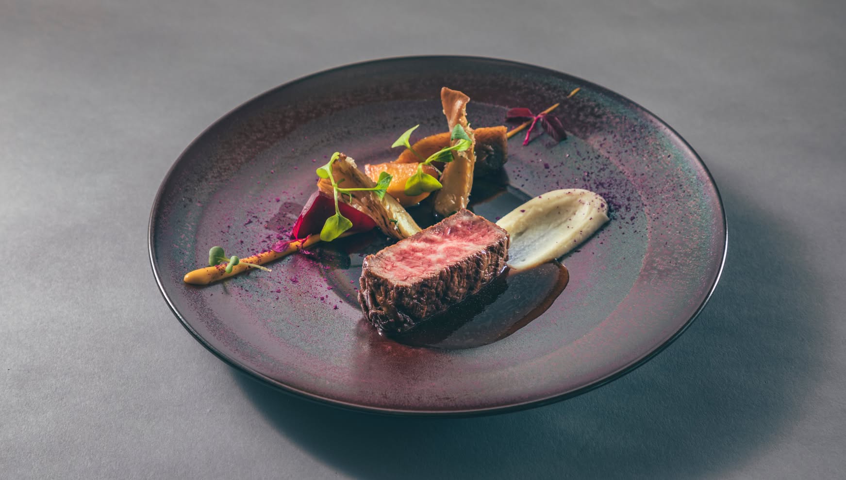 アイネス ヴィラノッツェ 沖縄で提供される、黒いシックな皿に盛り付けられた牛フィレ肉のロースト。絶妙な火入れの肉料理に、滑らかなピューレ、焼き野菜、スプラウトが添えられ、赤ワインソースと紫のパウダーが華を添えるウエディングのメインディッシュ。