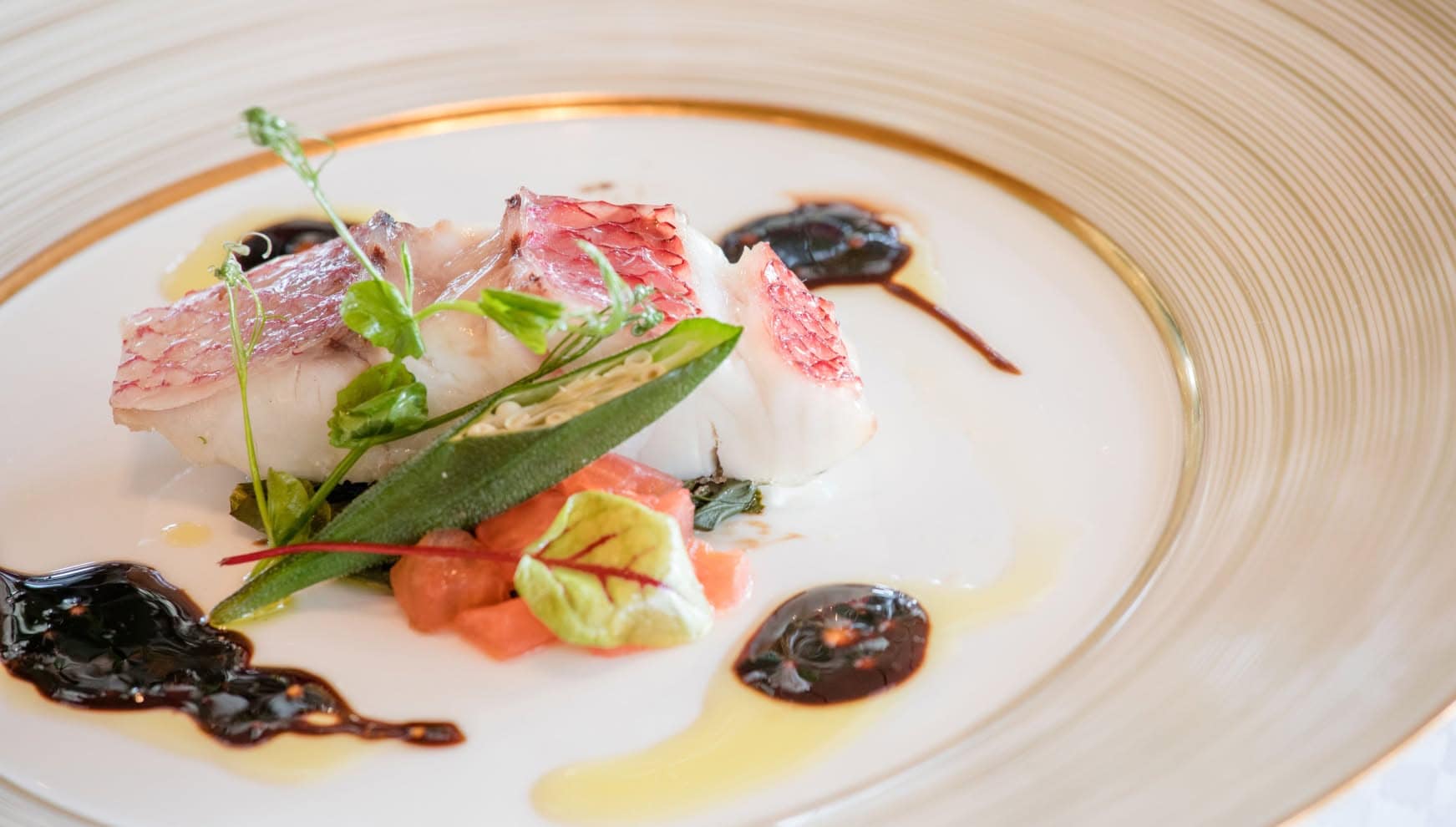 アイネス ヴィラノッツェ in カヌチャベイで提供される、鮮やかな赤色が映える真鯛のポワレ。しっとりと焼き上げられた白身魚に、オクラやトマトのグリルを添え、バルサミコソースとオイルのコントラストが美しい、リゾートウエディングを彩る一皿。