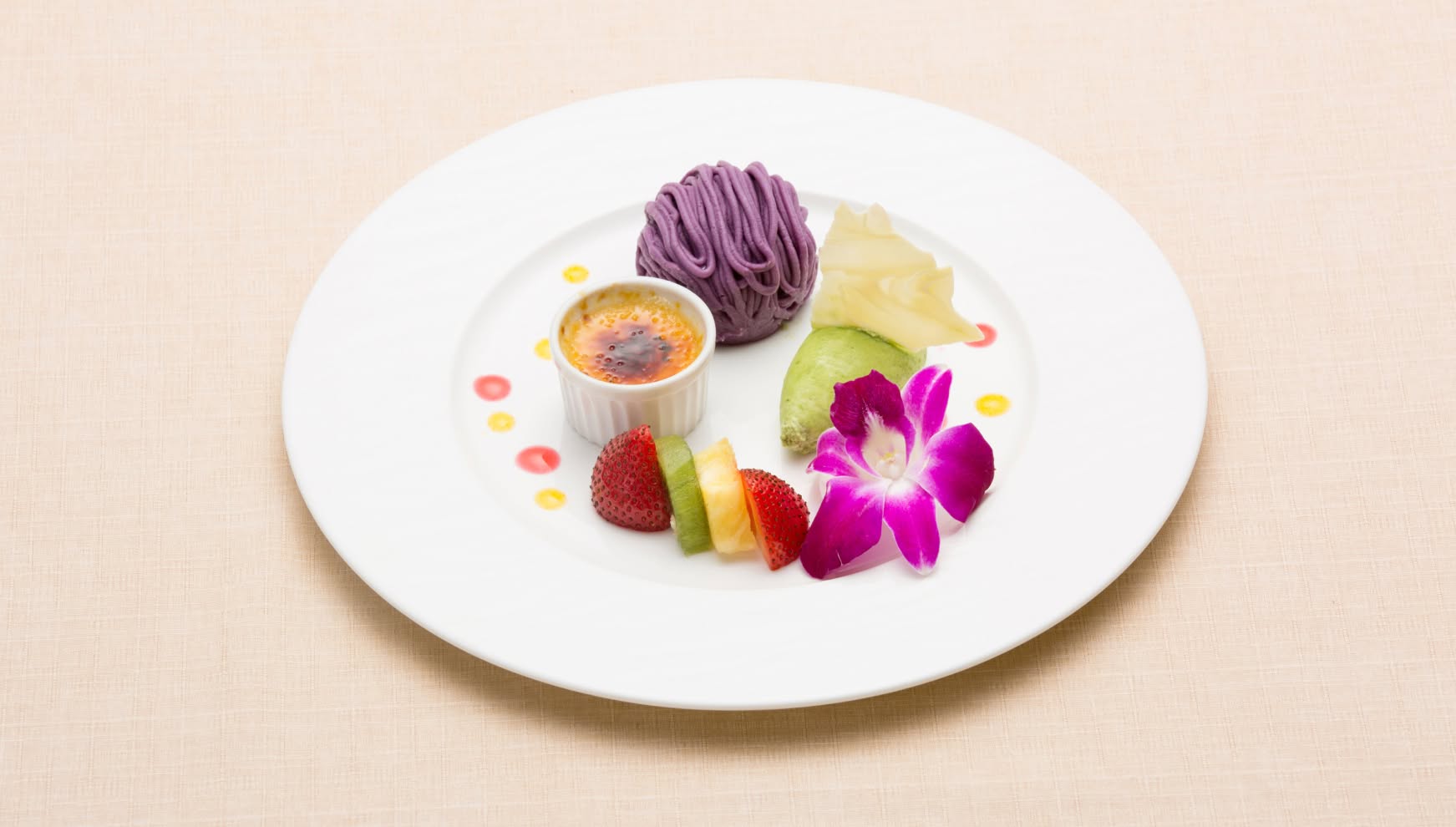 アイネス ヴィラノッツェ in カヌチャベイで提供される、沖縄の恵みを凝縮したデザートプレート。紅芋のモンブランやクレームブリュレ、季節のフルーツ、ピスタチオのアイスに鮮やかなデンファレを添えた、ウエディングの最後を彩る華やかな一皿。