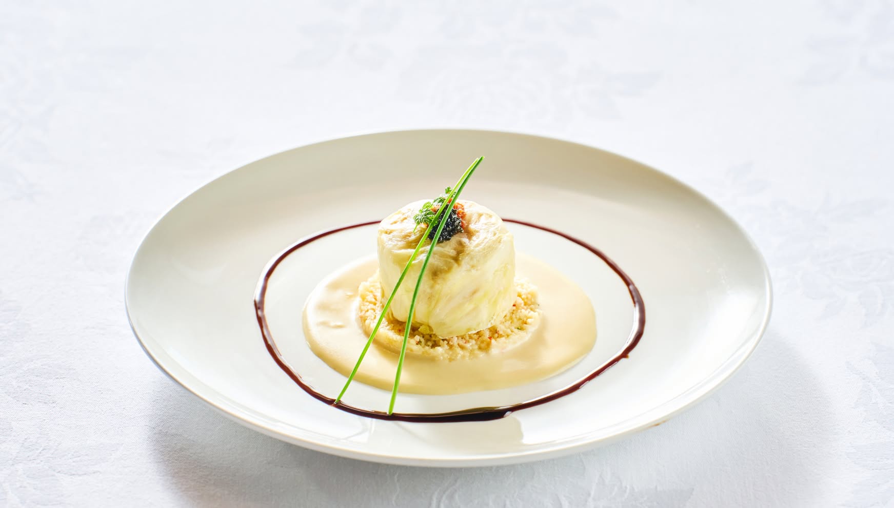 真っ白な丸皿の中央に美しく配置された、鮮魚のポワレのタルタル仕立て。キャビアとハーブが天面に飾られ、クリーミーなホワイトソースとバルサミコソースのラインが皿を彩る、ウエディングコースの上品な魚料理。
