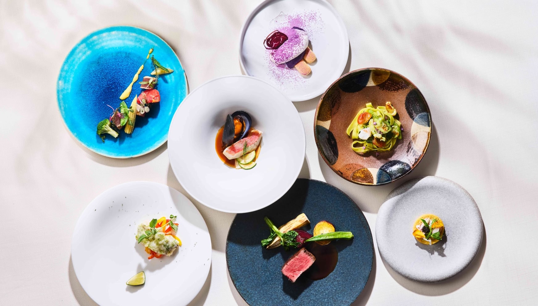 ザ・サーフビーチサイドテラスで提供される、色鮮やかな婚礼料理のフルコース。ターコイズブルーの皿に盛られた前菜、紅芋のデザート、厳選された肉料理やパスタなど、沖縄の自然と旬の味覚を五感で楽しむ、洗練されたおもてなしのメニュー。