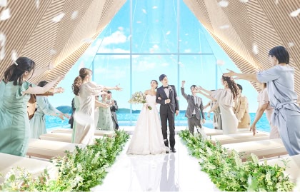 沖縄本島のザ・サーフ ビーチサイドテラスの挙式会場で、笑顔の参列者からフラワーシャワーの祝福を受けながらバージンロードを歩く新郎新婦