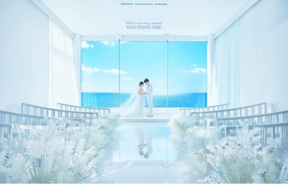 全面ガラス張りの窓から青い海と空が一望できる真っ白な挙式会場で、祭壇の前で向かい合って手を取り合う新郎新婦