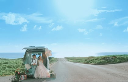 海へと続くまっすぐな一本道の脇に停めた、風船などでかわいく装飾されたレトロな車の荷台に腰掛け、リラックスした様子の新郎新婦