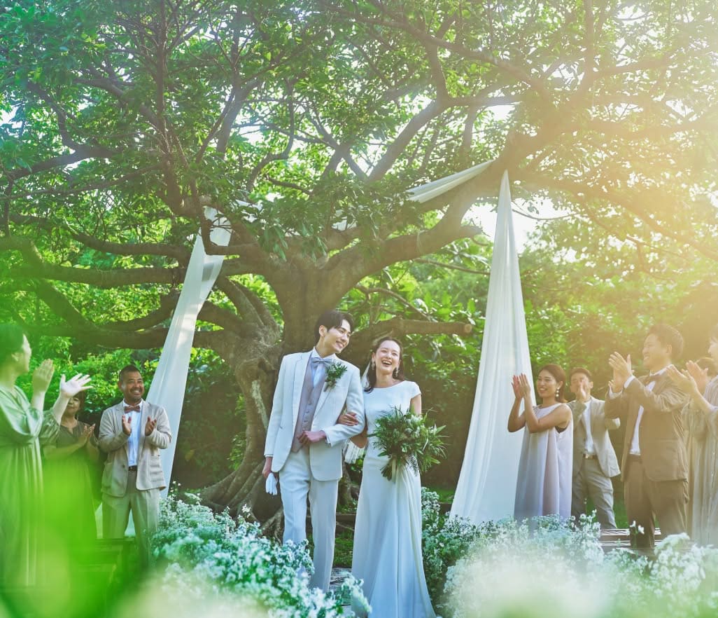 沖縄の緑豊かな自然に囲まれたガーデンウエディングで、幸せそうに微笑む新郎新婦と参列者たち