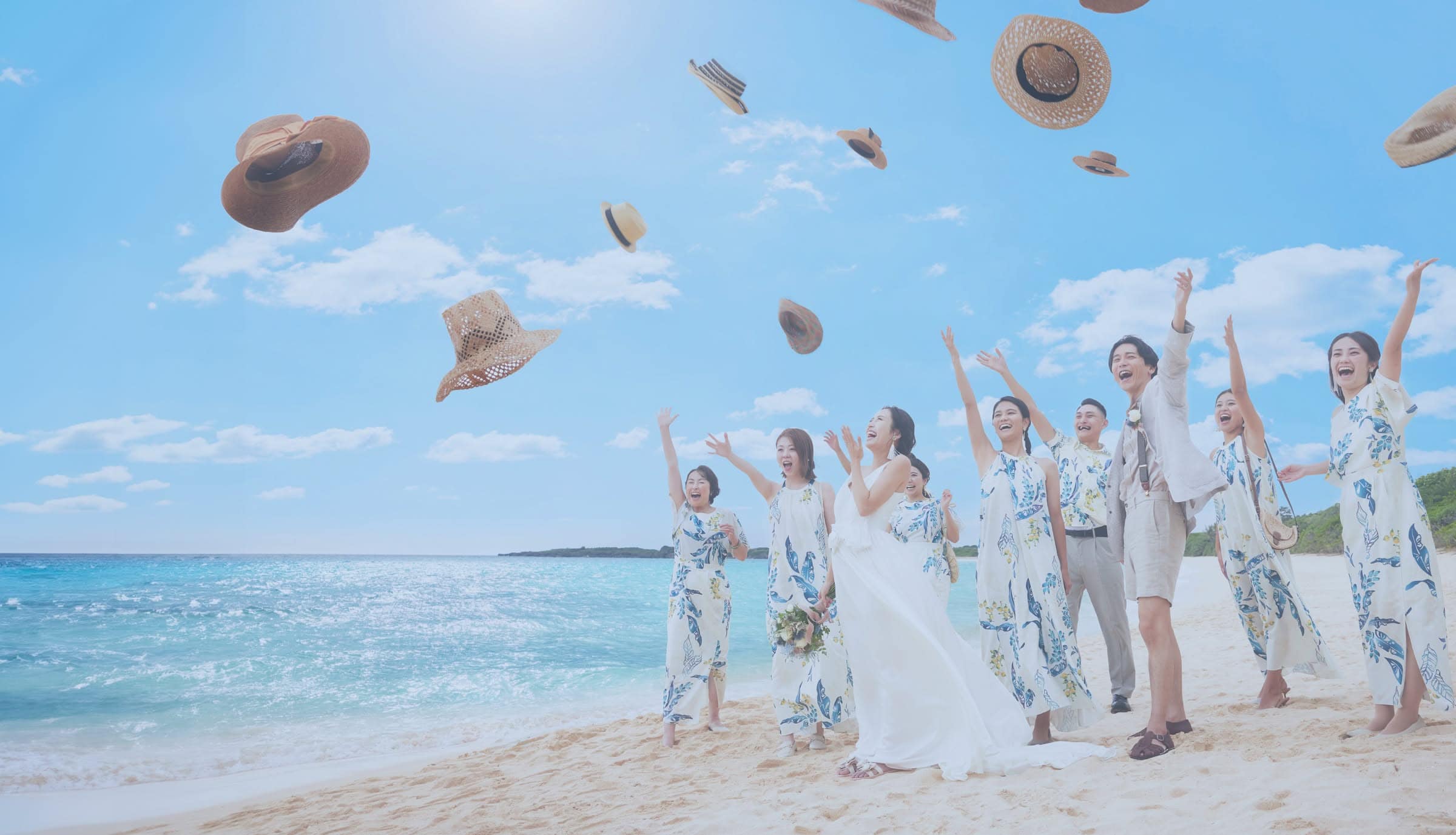 真っ青な空と白い砂浜が広がるビーチで、新郎新婦とゲスト全員が麦わら帽子を一斉に空へ投げて祝福するウエディングフォト。お揃いのかりゆしワンピースを着た友人たちと共に、開放感あふれる沖縄のロケーションで喜びを表現した陽気でダイナミックなシーンです。