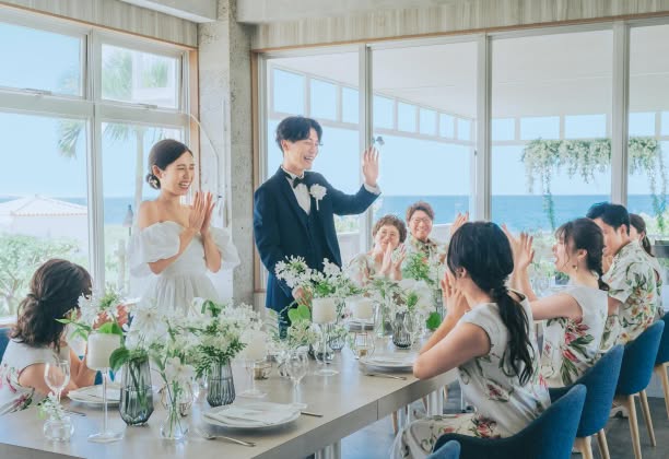 会食会場でお揃いのかりゆしウェアを着たゲストに新郎新婦が挨拶をしている様子、新郎新婦は笑顔でゲストに感謝の気持ちを伝え、楽しい時間を過ごしています。ゲストも新郎新婦の挨拶に応え、温かい拍手や笑顔で祝福しています。会場は和やかな雰囲気に包まれ、皆が一緒に楽しんでいる様子が伝わってきます。