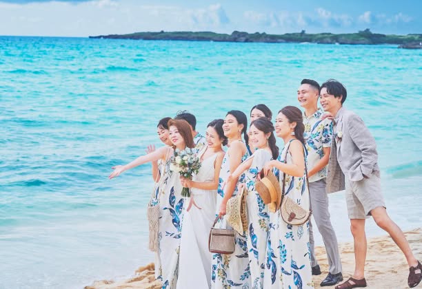 透き通る青い海と空の下、お揃いのかりゆしウェアを纏ったゲストと新郎新婦が海を眺めているウエディングフォト。