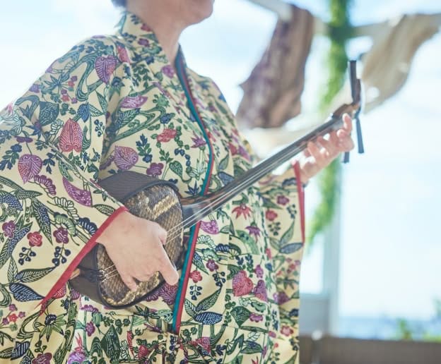 明るい陽光が差し込むチャペル内で、かりゆしウェアを着用した父親と腕を組み、満面の笑みを浮かべてバージンロードを歩む新婦のウエディングフォト。白い胡蝶蘭のブーケを手に、幸せ溢れる表情で一歩を踏み出す感動的な挙式シーンの一枚です。