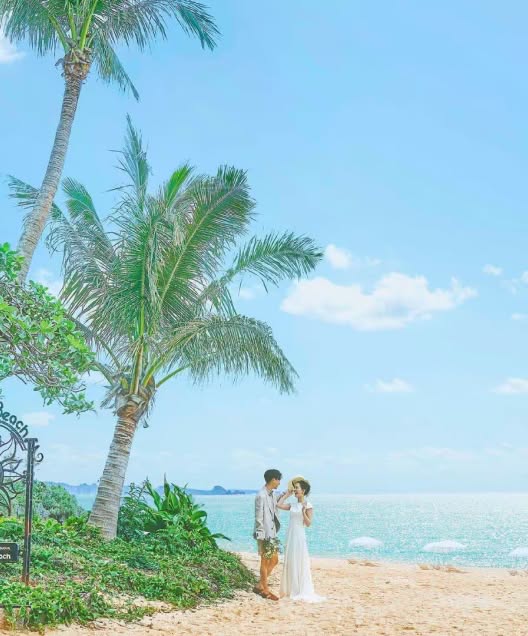 沖縄の海を望む開放的なテラスでのウエディングパーティー。白いタキシードとウエディングドレス姿の新郎新婦が笑顔で入場し、ゲストが拍手で祝福する様子。背景には青い海とヤシの木が広がり、南国らしい披露宴の情景です。