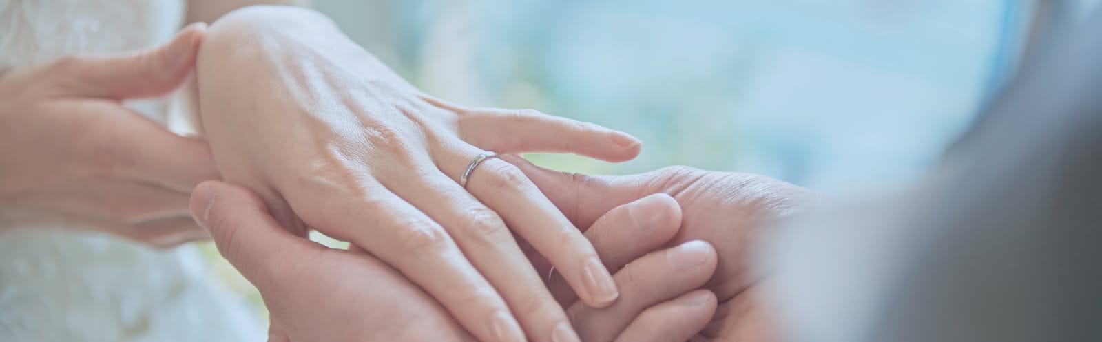 ウエディングの挙式にて、新郎が新婦の薬指に結婚指輪をはめる指輪交換のシーンのアップ。柔らかい自然光が手元を照らし、シンプルで洗練されたデザインの指輪が輝く。誓いの瞬間を象徴する、情緒的で温もりのあるコラム用画像。