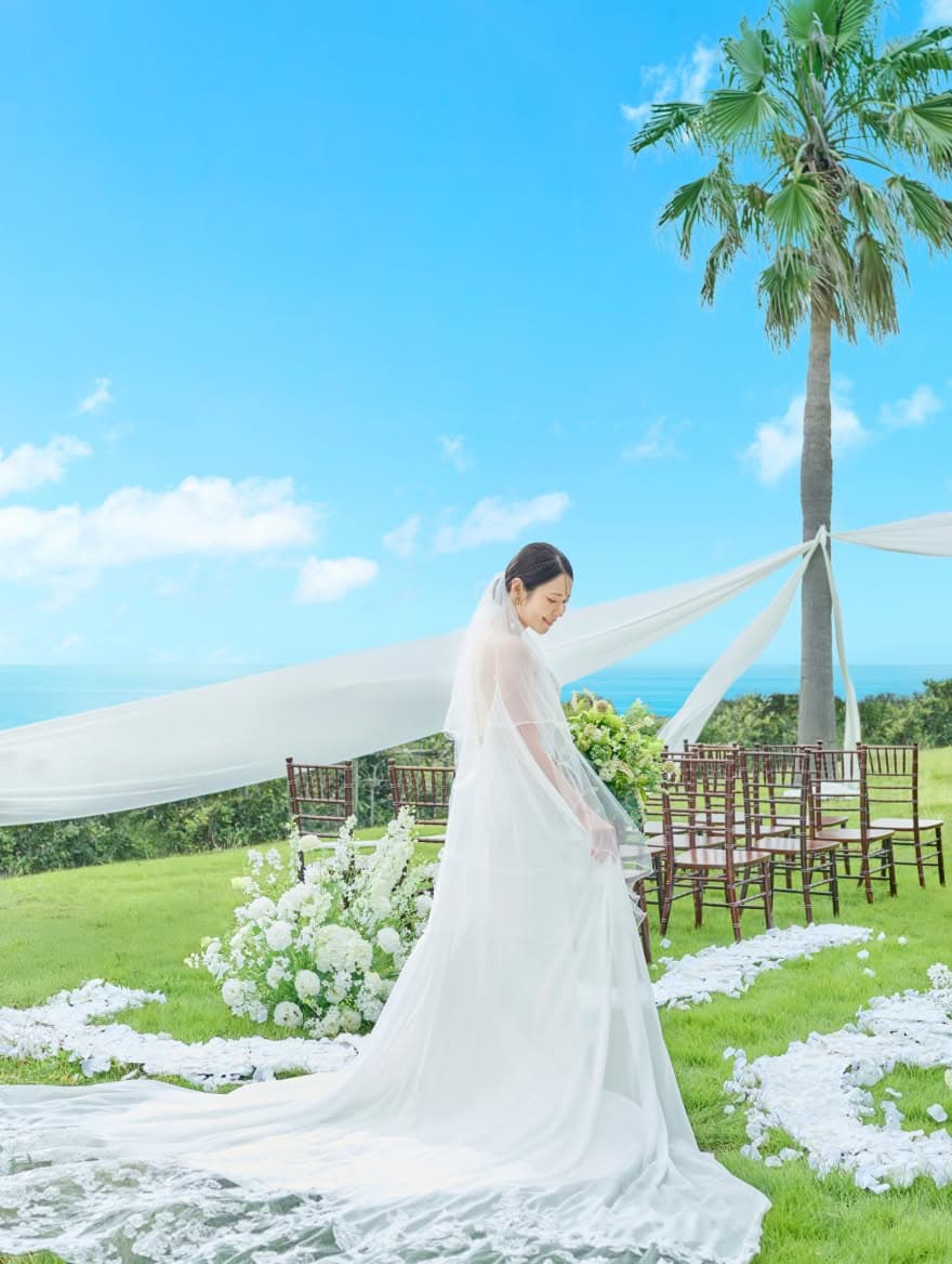 沖縄の青空の下、緑豊かなガーデンでウエディングドレスを着て幸せそうに微笑む花嫁