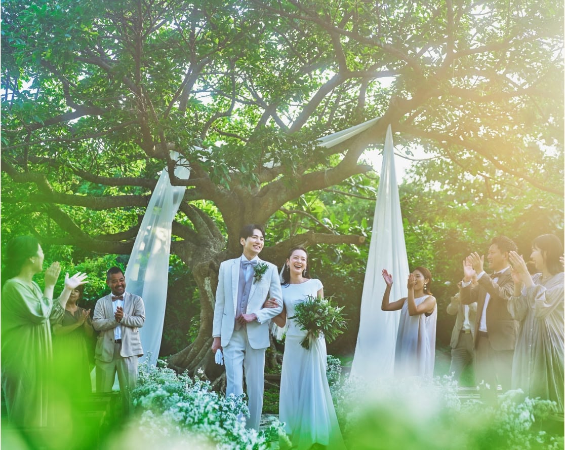沖縄の緑豊かな自然に囲まれたガーデンウエディングで、幸せそうに微笑む新郎新婦と参列者たち