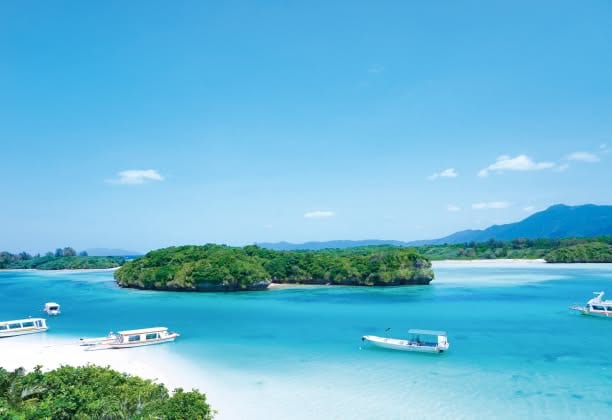 石垣島を代表する景勝地「川平湾」の絶景。世界的なガイドブックで三ツ星を獲得した、エメラルドグリーンのグラデーションが美しい海に、緑豊かな小さな島々が点在する。白い砂浜にはグラスボートが並び、背後には石垣島の山並みが広がる「一生ものの思い出」にふさわしいロケーション。