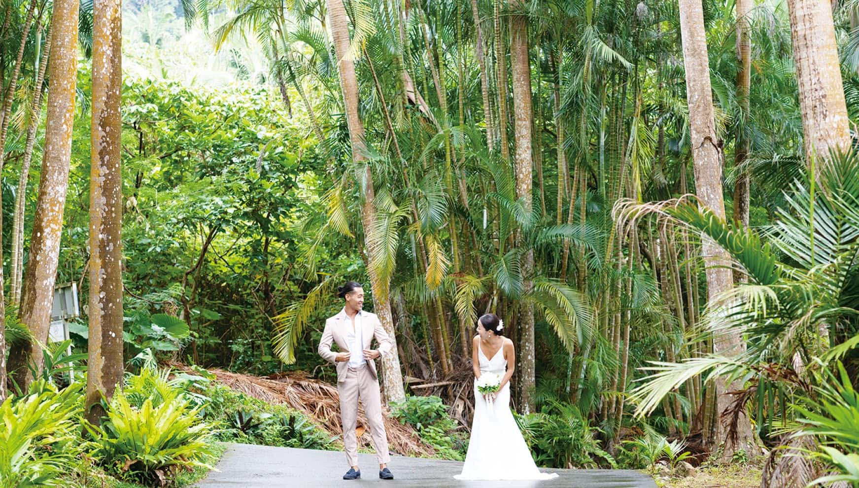 石垣島の天然記念物「米原ヤエヤマヤシ群落」の巨大なヤシの木々に囲まれた一本道で、笑顔を見せ合う新郎新婦。高くそびえ立つヤシの幹と鮮やかな亜熱帯の緑が、まるでジャングルのような迫力あるロケーションを演出する、石垣島ならではのネイチャーフォト。