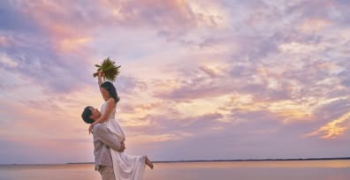 夕焼けに染まるドラマチックな空の下、新郎が新婦を高く抱きかかえるウエディングフォト。新婦はブーケを掲げ、二人の喜びが溢れる感動的なシーンを捉えています。静かな海を背にしたサンセットロケーションが、二人のシルエットを美しく引き立てる一枚です。