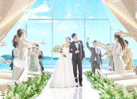 沖縄本島のザ・サーフ ビーチサイドテラスの挙式会場で、笑顔の参列者からフラワーシャワーの祝福を受けながらバージンロードを歩く新郎新婦