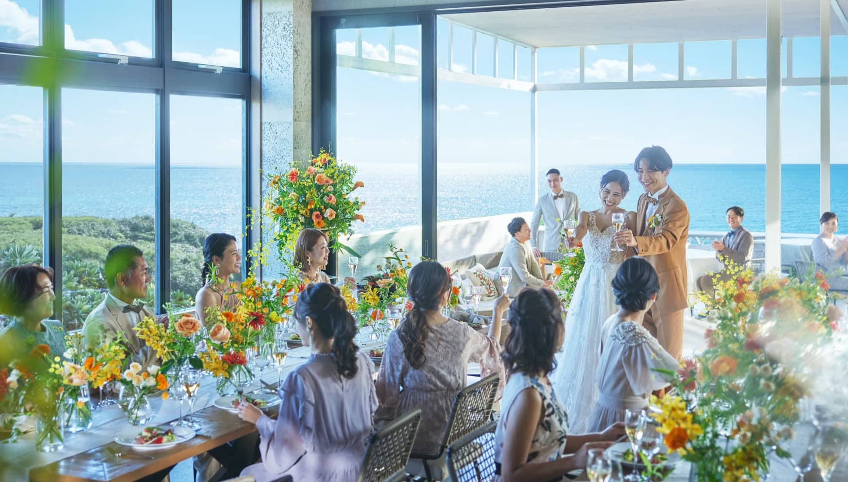 沖縄の海を背景にテラスで披露宴を行う新郎新婦とゲストの皆様