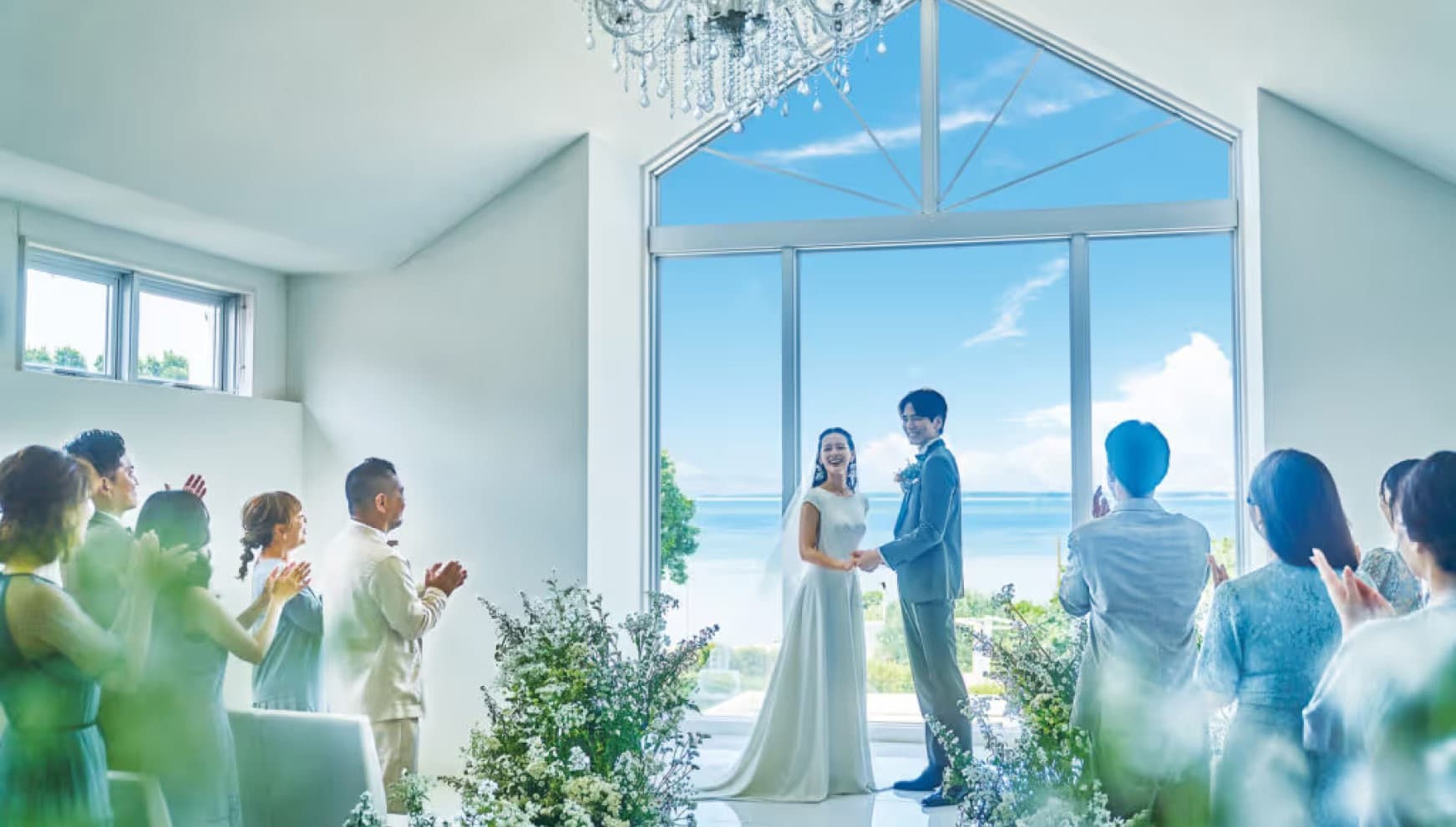 ザ・ビーチテラス ホテルアオ石垣のチャペルで、海を背景に新郎が新婦のベールを上げるベールアップの儀式。全面ガラス張りの向こうに石垣島の青い海が広がる、光に満ちた感動的な挙式の瞬間。