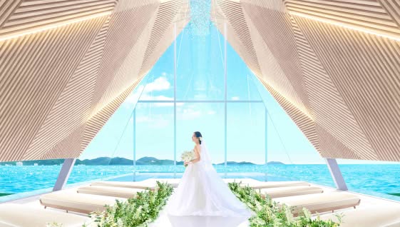 オーシャンビューが広がる「ザ・サーフビーチサイドテラス」のチャペルで、祭壇に立つウエディングドレス姿の新婦。木組みの幾何学的な天井デザインと、青い海と空が一体化する開放的な空間が特徴的なウエディングシーン。