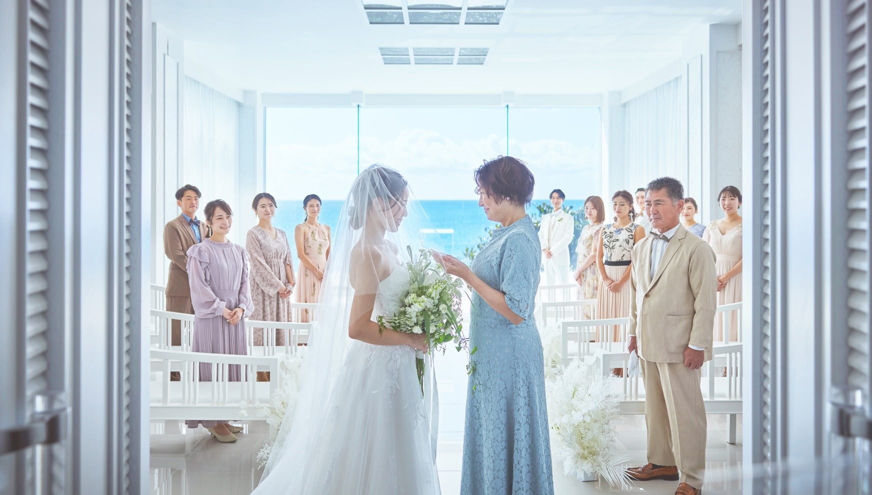 ザ・サーフ シーサイドシーン宮古島のチャペルで、挙式前に母親からベールダウンを受ける新婦の様子。青い海を背景に、家族やゲストが見守る温かな雰囲気の中、ウエディングドレス姿の新婦が感謝を伝える感動的なシーン。