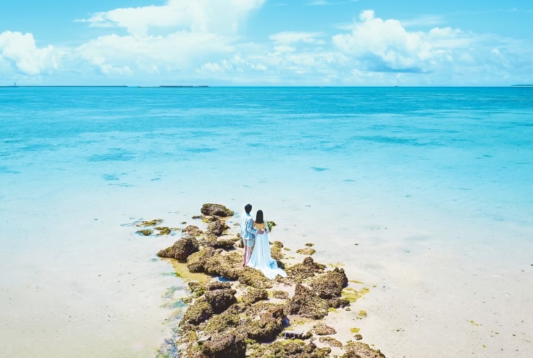 ビーチにある岩場に立ち、ウエディングフォトの撮影ポーズをとる新郎新